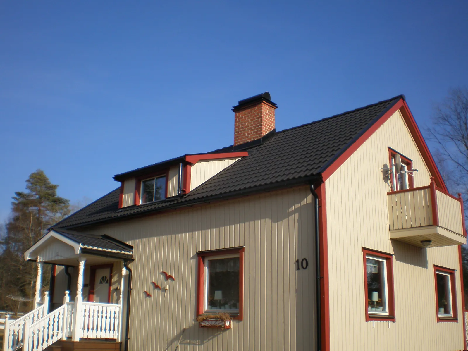 Renoverat trähus med ljus fasad, röda knutar och svart tak