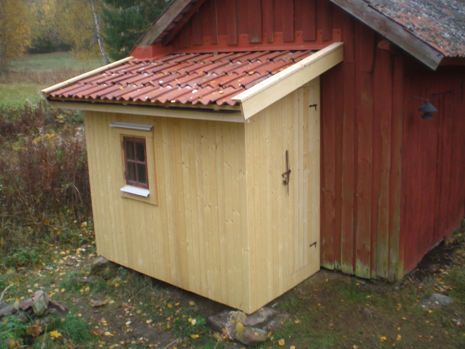 Mindre tillbyggnad med ljus träpanel och rött tegeltak